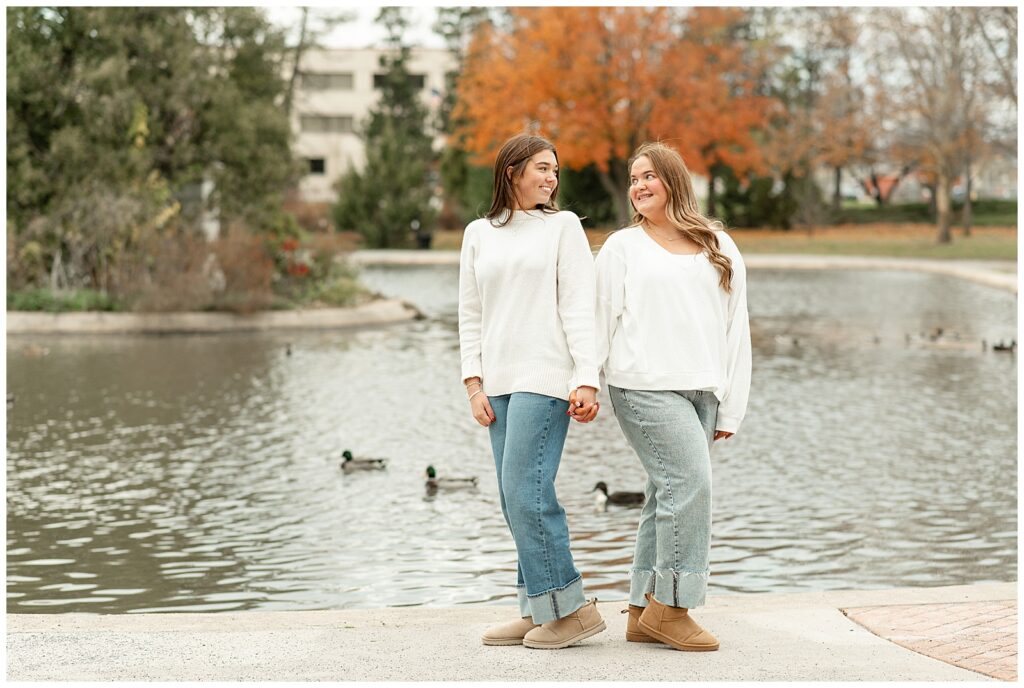 two senior girls holding hands by pond with ducks for this Fall Senior Team Session in York PA