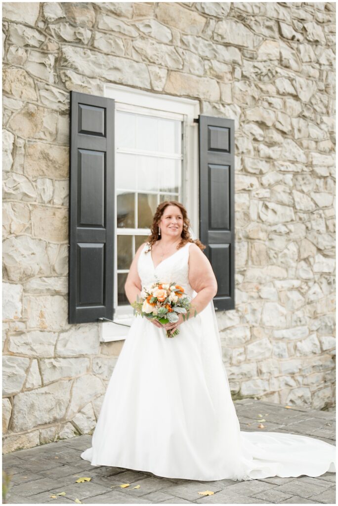 bride in white sleeveless gown holding orange and white bouquet for this Barn at Silverstone Fall Wedding