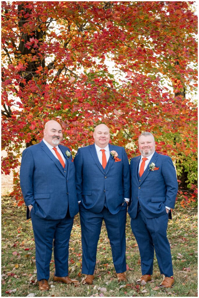 groom with his two groomsmen all in navy suits with orange ties for this Barn at Silverstone Fall Wedding