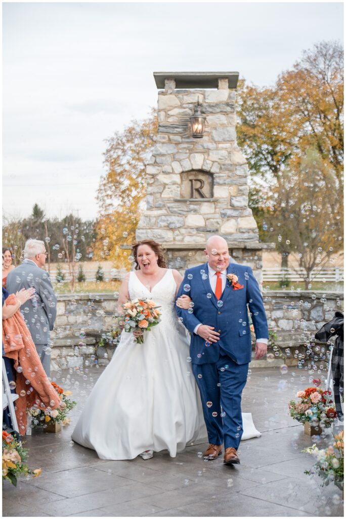 couple smiling as they leave wedding ceremony through cloud of bubbles for this Barn at Silverstone Fall Wedding