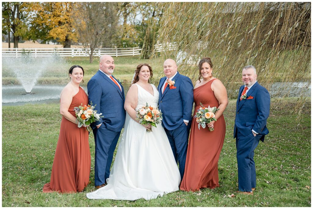 couple with their bridal party by willow tree and pond for this Barn at Silverstone Fall Wedding