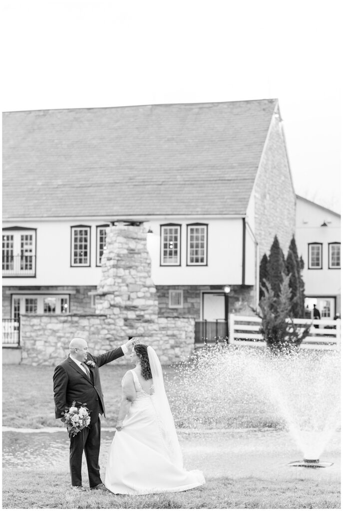 black and white photo of groom twirling his bride by pond and barn for this Barn at Silverstone Fall Wedding