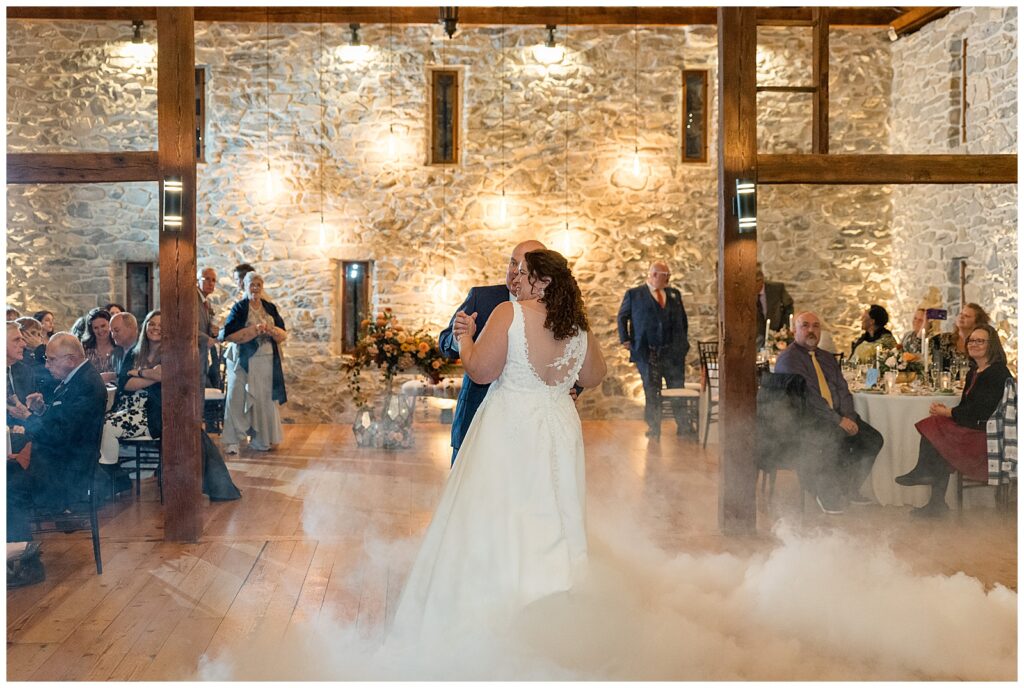 couple sharing their first dance with smoky floor as guests watch for this Barn at Silverstone Fall Wedding