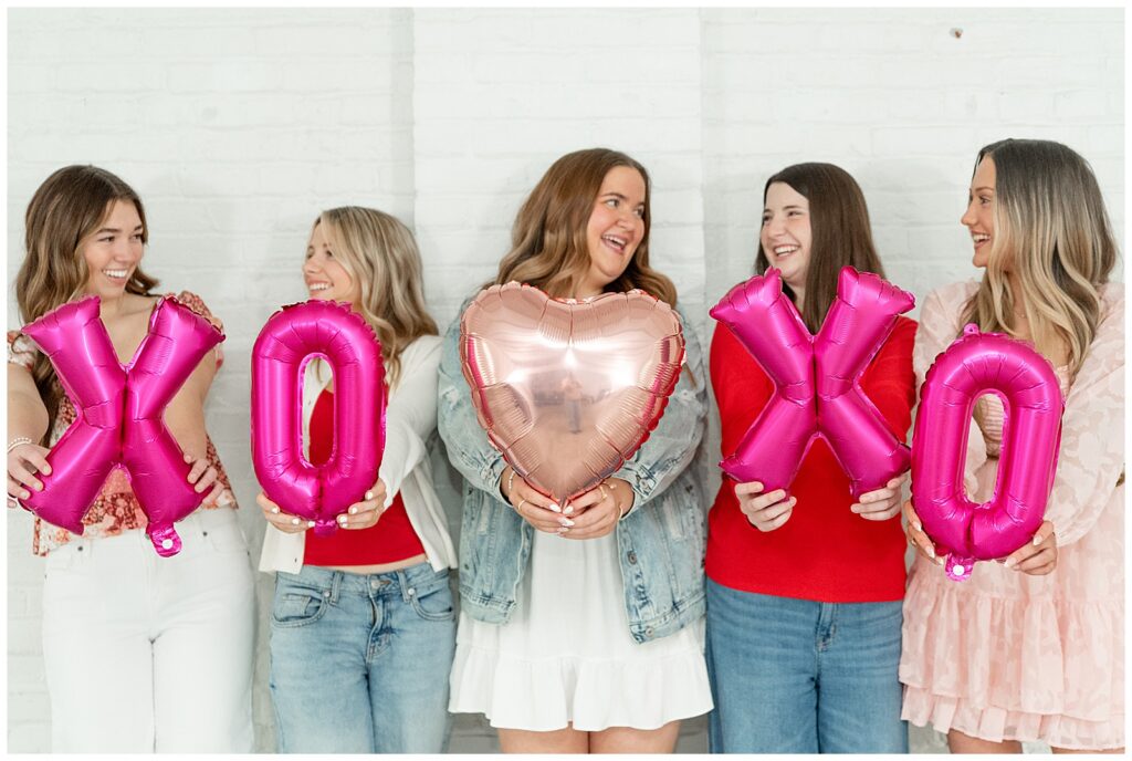 senior girls holding valentines balloons toward camera at the white room in lancaster pa for this Valentines Day BFF Shoot