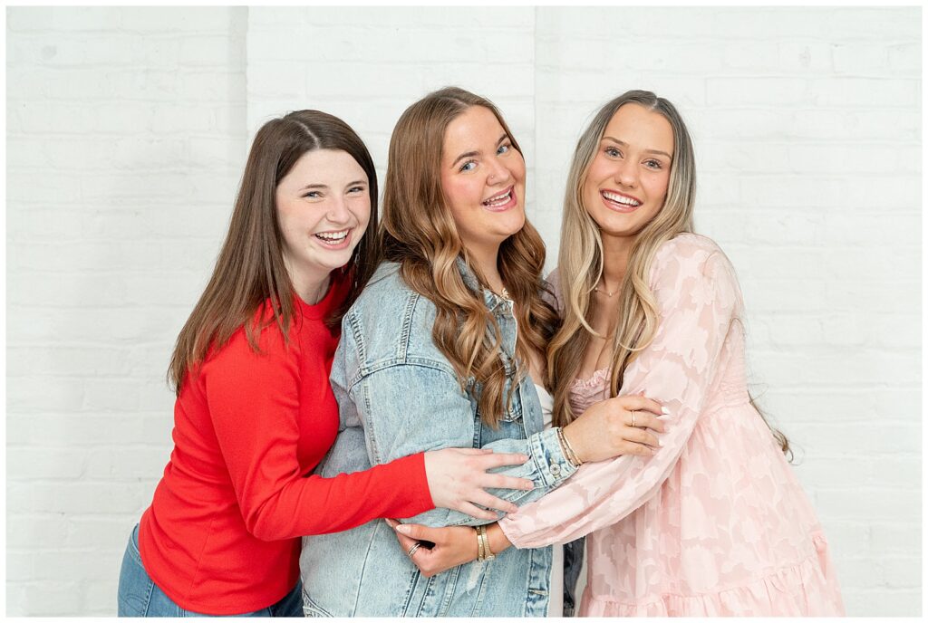 three senior girls standing close and hugging in shades of red and pink for this Valentines Day BFF Shoot