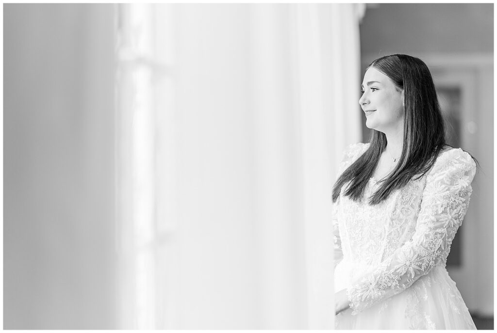 black and white image of bride looking out window with sheer curtain for this Wedding at The Rotunda at Lauxmont Farms