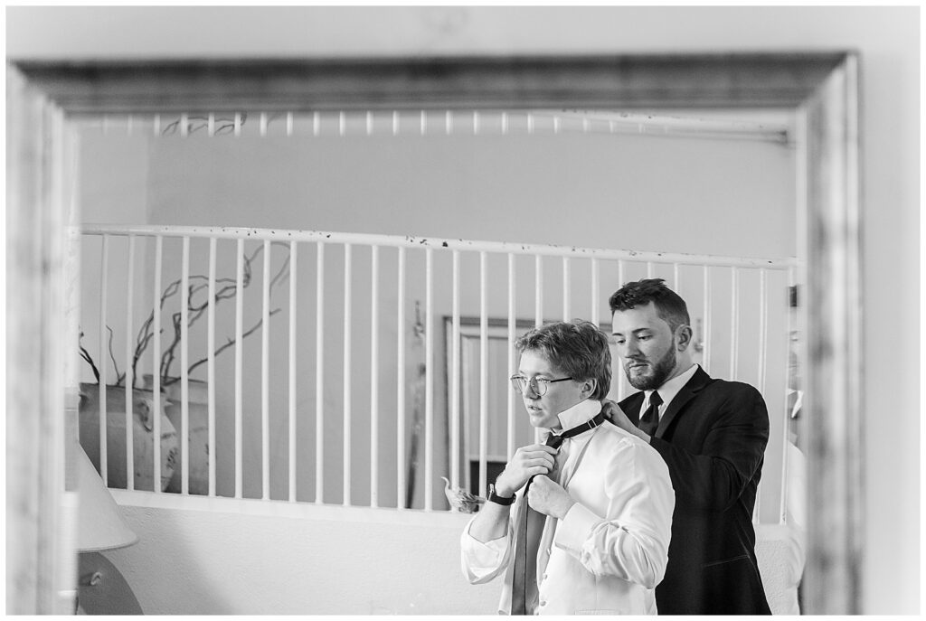 black and white image of best man and groom working to get his tie ready for this Wedding at The Rotunda at Lauxmont Farms