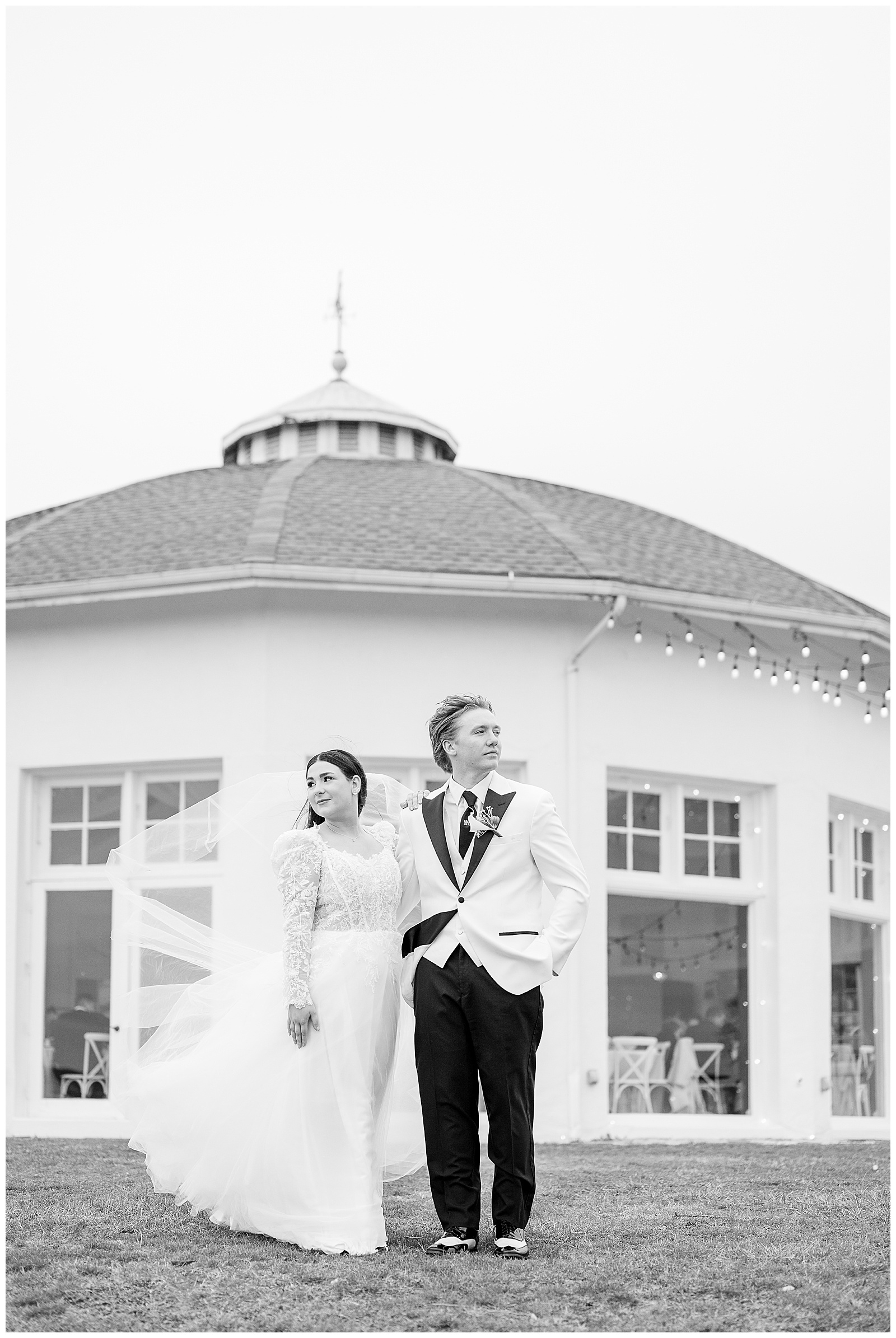black and white image of couple holding hands and looking in opposite directions by round building for this Wedding at The Rotunda at Lauxmont Farms