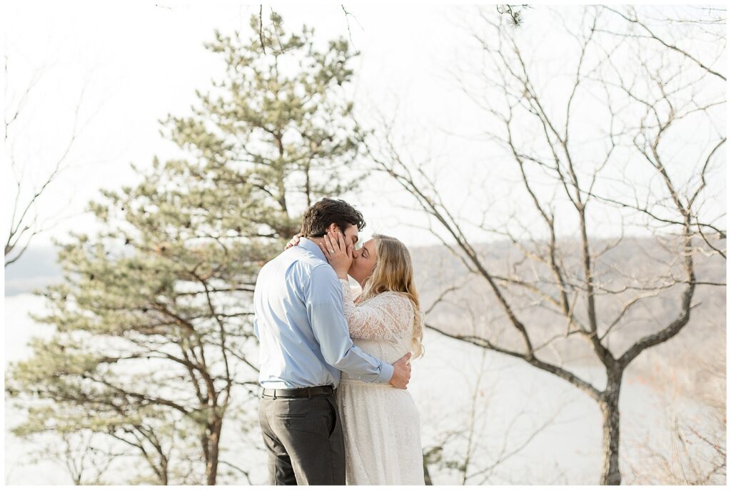 couple standing on cliff and kissing by susquehanna river for this Pinnacle Point Spring Engagement Session
