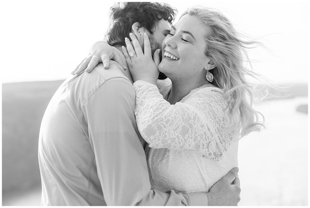 black and white photo of guy kissing girls right cheek as she hugs his face for this Pinnacle Point Spring Engagement Session