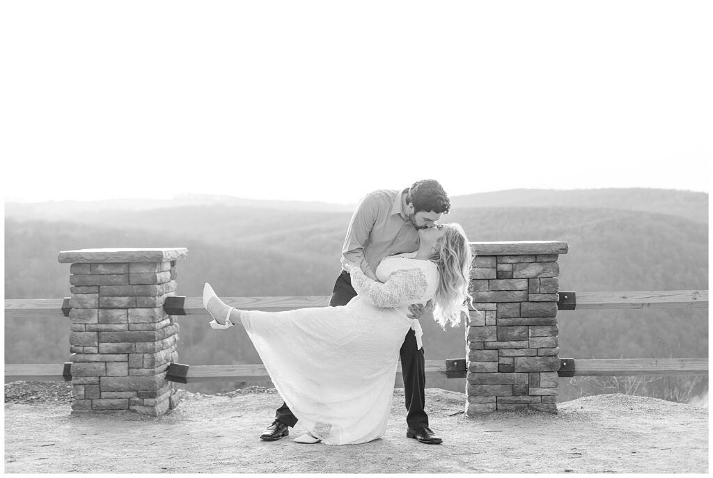 black and white photo of man dipping woman back and kissing her at fenced overlook for this Pinnacle Point Spring Engagement Session
