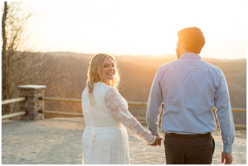 couple holding hands walking away from camera as bride looks back for this Pinnacle Point Spring Engagement Session