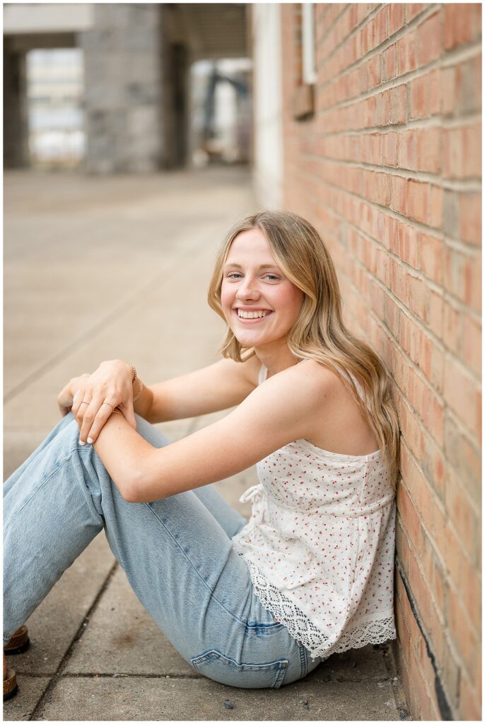 girl sitting with knees bent leaning back against brick wall at her spring founders hall senior session