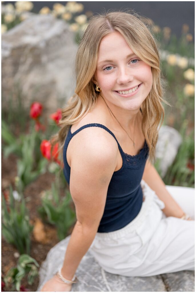 senior in navy blue spaghetti strap shirt and linen white pants sitting with tulips all around