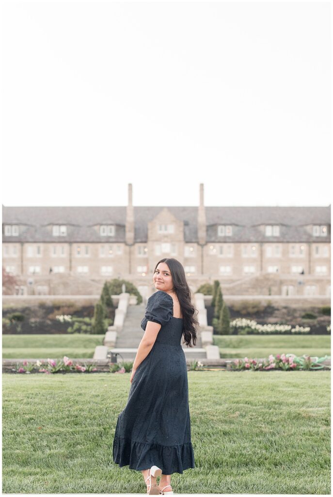 senior girl with back to camera and looking back over left shoulder with beautiful building behind her for this Spring Masonic Village Senior Session