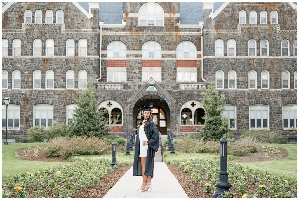 Moravian University graduate wearing cap and gown standing in front of building on campus