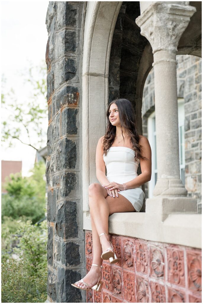 senior sitting in stone arch opening with white dress on