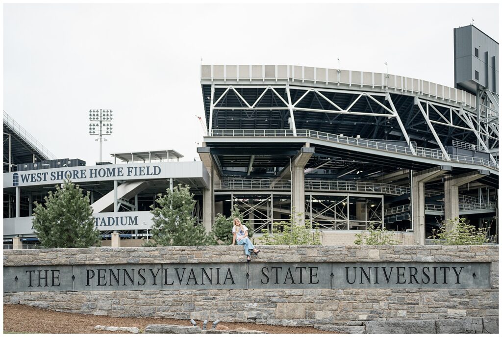 girl graduate sitting on The Pennsylvania State University sign in front of Beaver Stadium