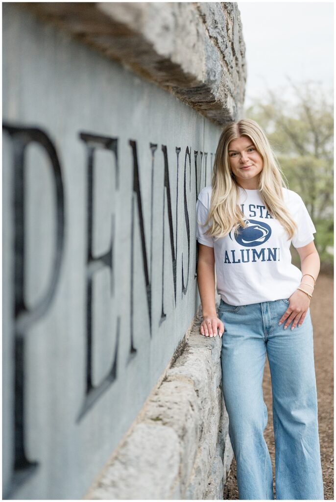 college grad leaning against Penn State sign in front of Beaver Stadium