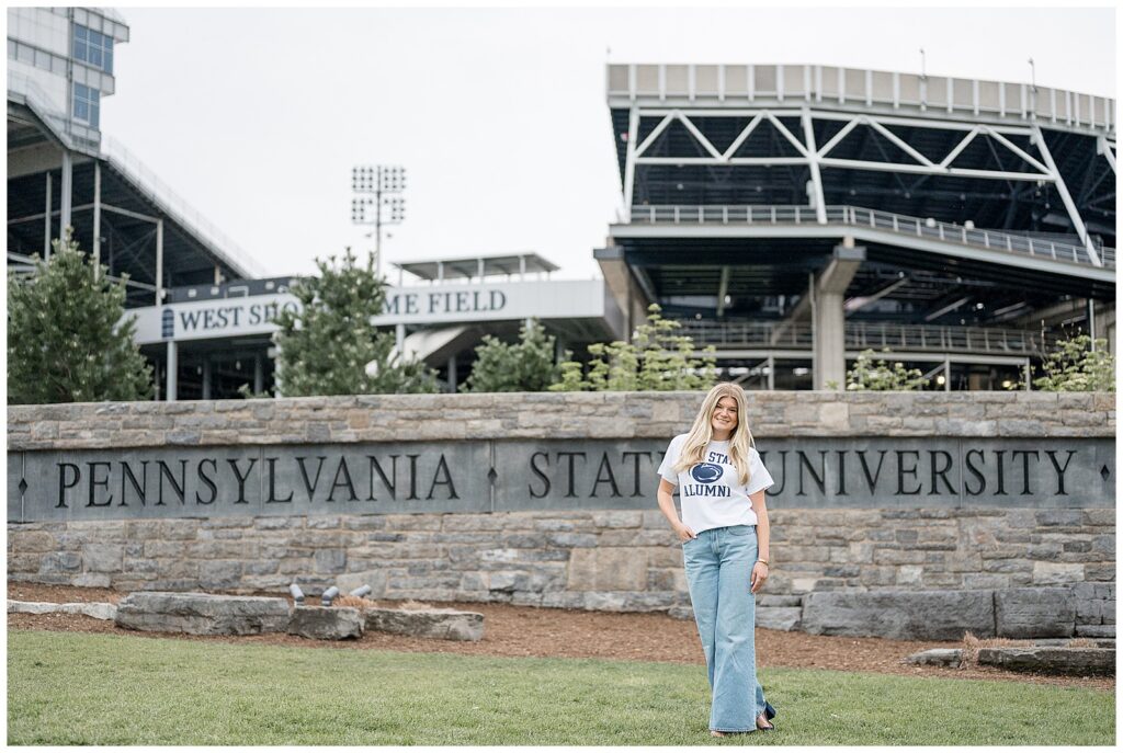 Penn State graduate standing in front of Beaver Stadium with Alumni shirt on