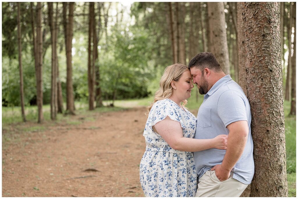 guy leaning on tree while couple rests foreheads together 