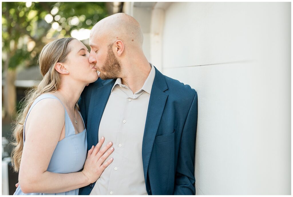 Engaged couple kissing against a white wall in downtown Lancaster Pennsylvania during a golden hour engagement session