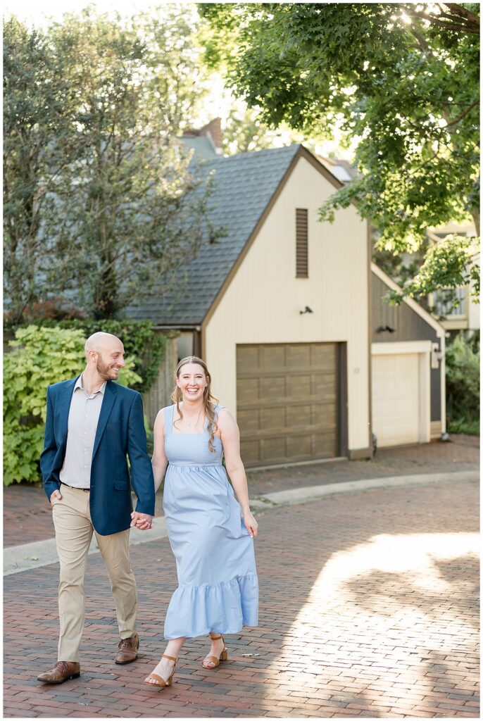 Engaged couple walking hand in hand and laughing on a brick street in downtown Lancaster PA, candid engagement photo by Heather Marie Photography