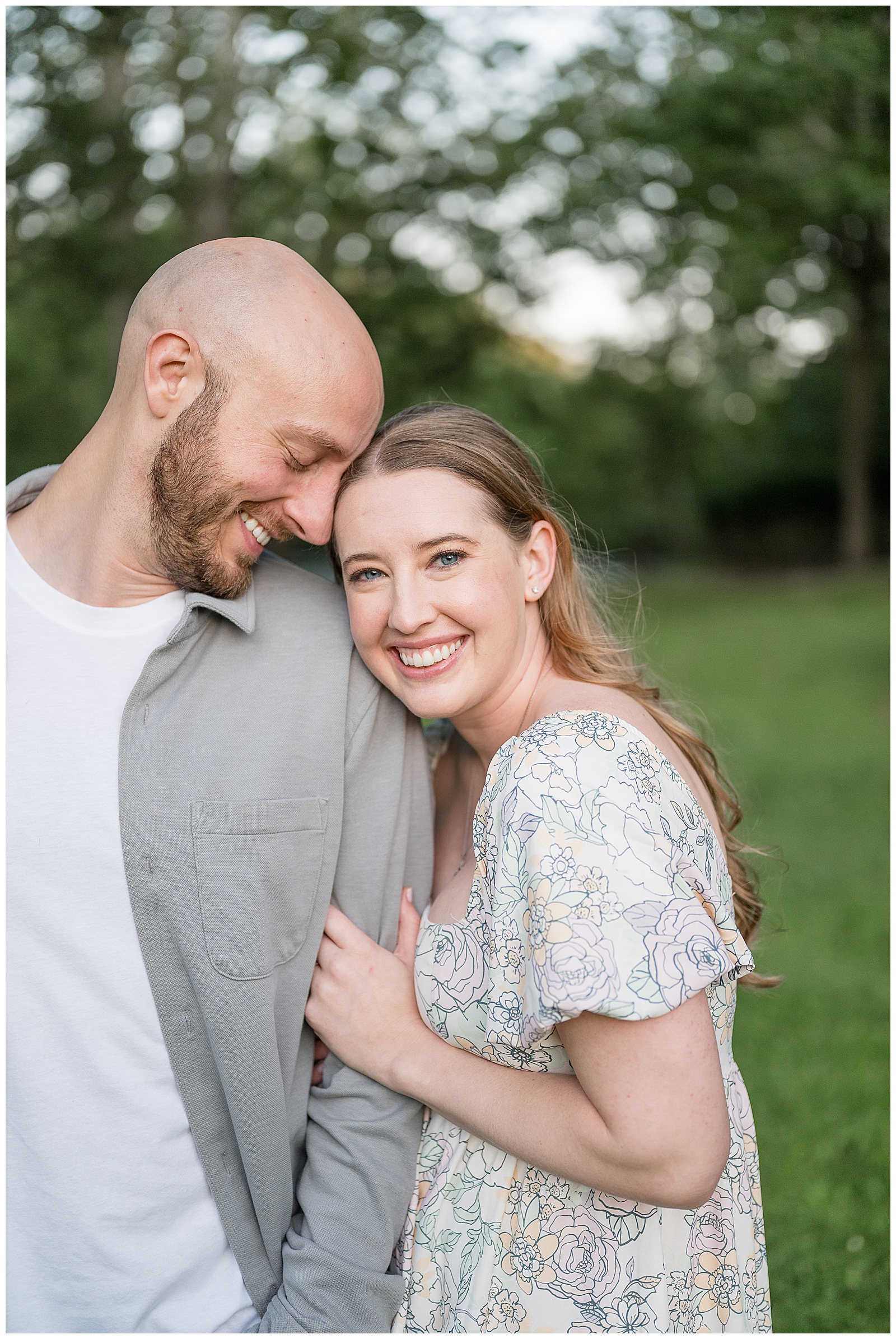 Engaged couple snuggled close and smiling in a bright outdoor portrait at Lancaster County Central Park PA, light and airy engagement photography