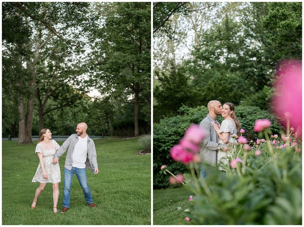 Engaged couple walking through green grass and sharing a kiss near blooming pink peonies at Lancaster County Central Park, Lancaster PA engagement photographer