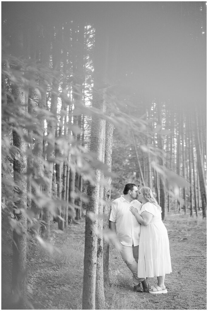 Black and white engagement portrait of couple kissing against a pine tree at Overlook Park Lancaster PA, timeless engagement photography by Heather Marie Photography