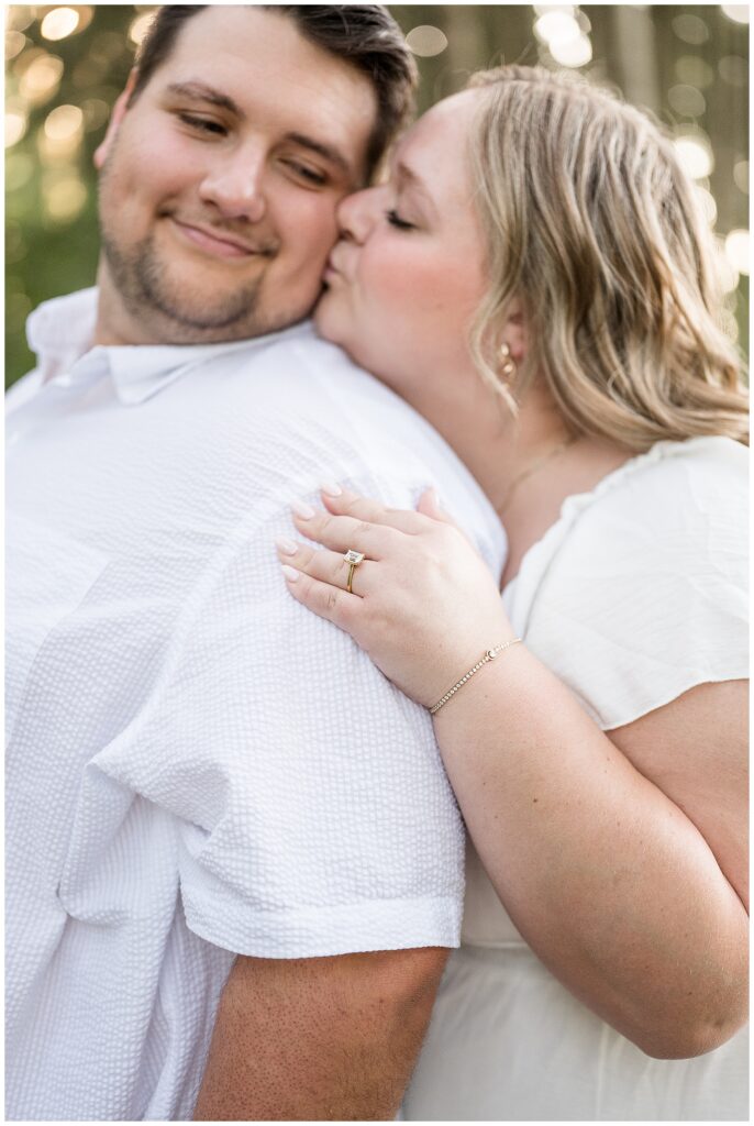 Close-up engagement portrait showing fiancée's emerald cut diamond ring as she kisses her partner's cheek in the pine grove at Overlook Park Lancaster PA