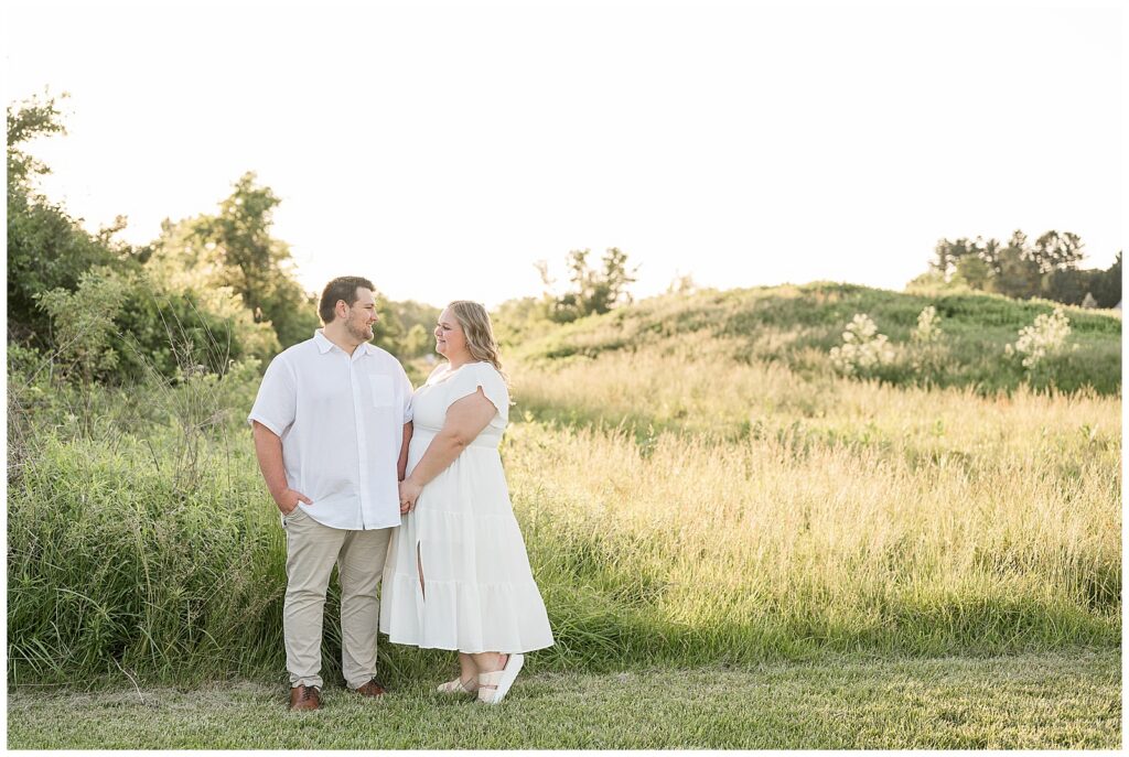 Engaged couple holding hands and smiling at each other in a sun-drenched wildflower meadow at Overlook Park Lancaster PA, engagement photographer Heather Marie Photography