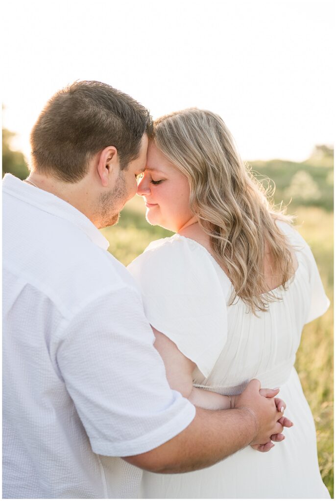 Engaged couple touching foreheads and embracing in a glowing summer field at Overlook Park in Lancaster Pennsylvania, soft golden hour engagement portrait by Heather Marie Photography