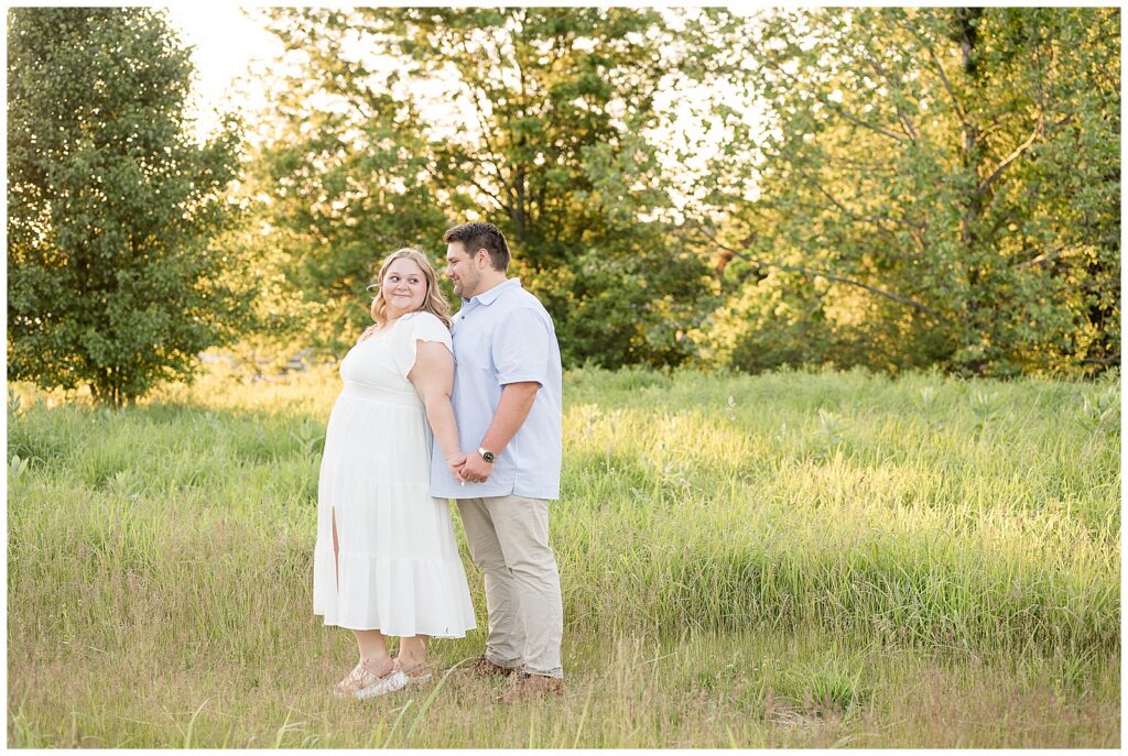 Engaged couple holding hands and smiling in a lush green field at Overlook Park Lancaster PA during their summer sunset engagement session