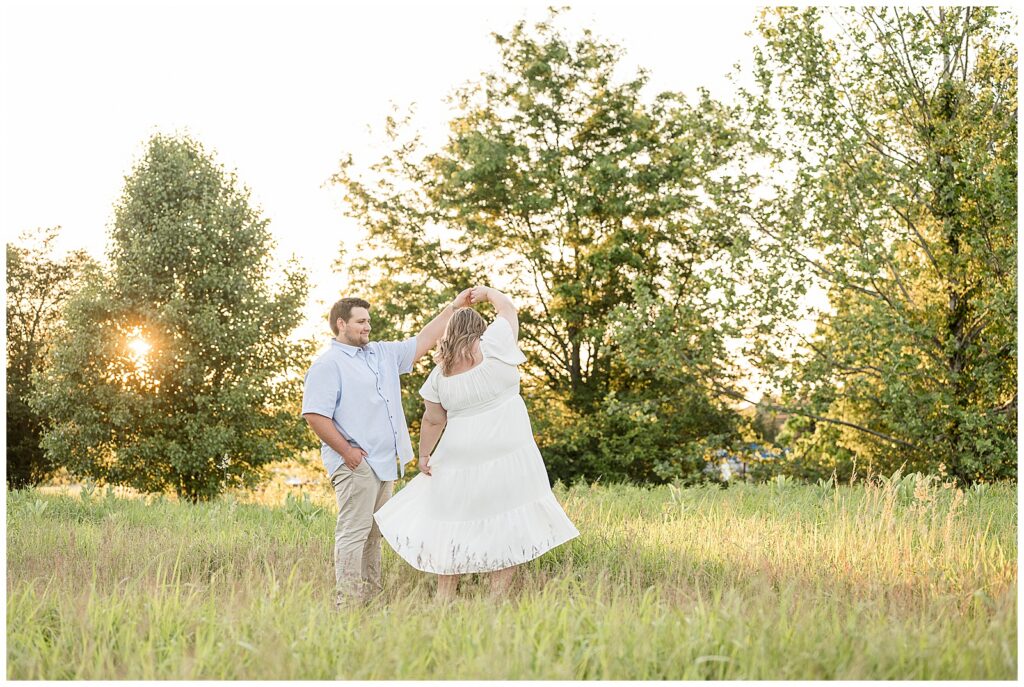 Man spinning his fiancée in a wide open meadow at sunset at Overlook Park Lancaster Pennsylvania, playful golden hour engagement photography by Heather Marie Photography