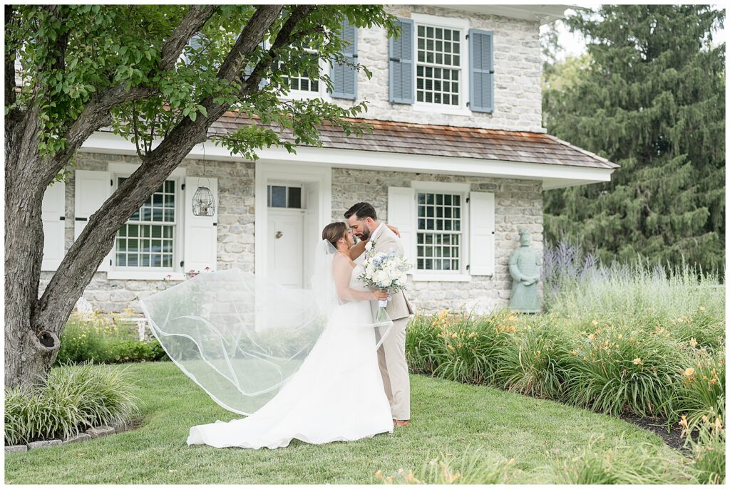 Bride and groom sharing a kiss with her cathedral veil blowing in the summer breeze during portraits at Bluestone Estate | Heather Marie Photography