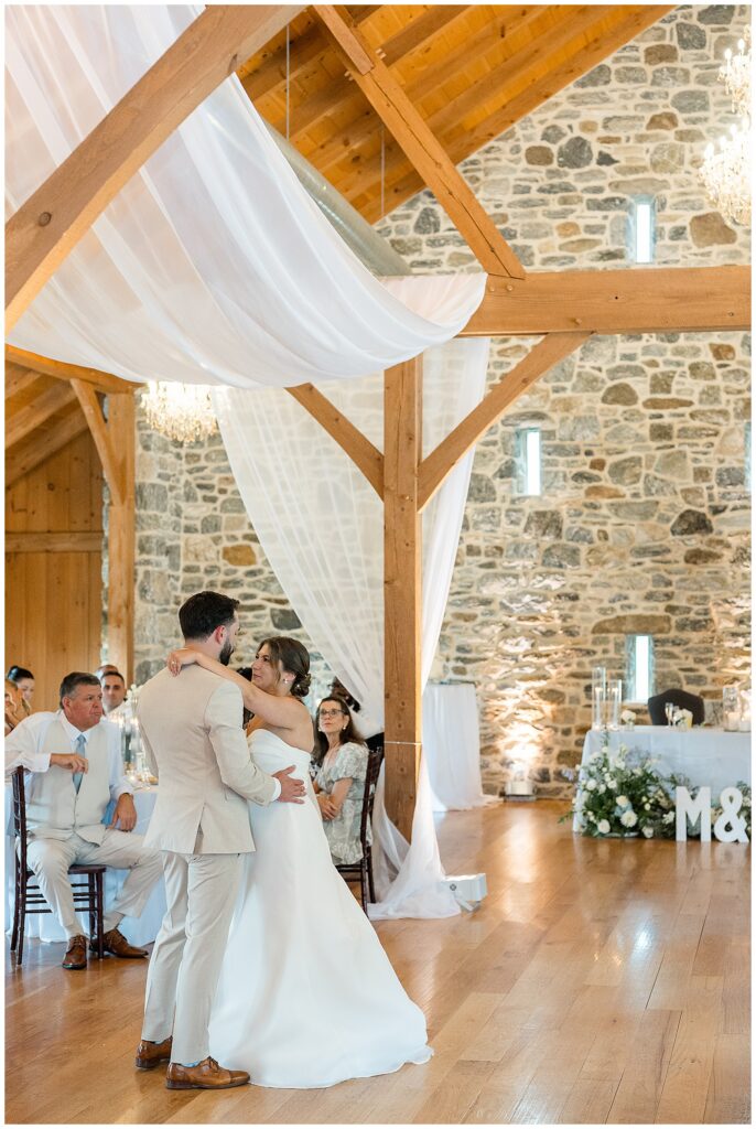 Bride and groom sharing their first dance in the stone reception barn at Bluestone Estate, with white draping overhead and the M&Z marquee letters in the background | Heather Marie Photography