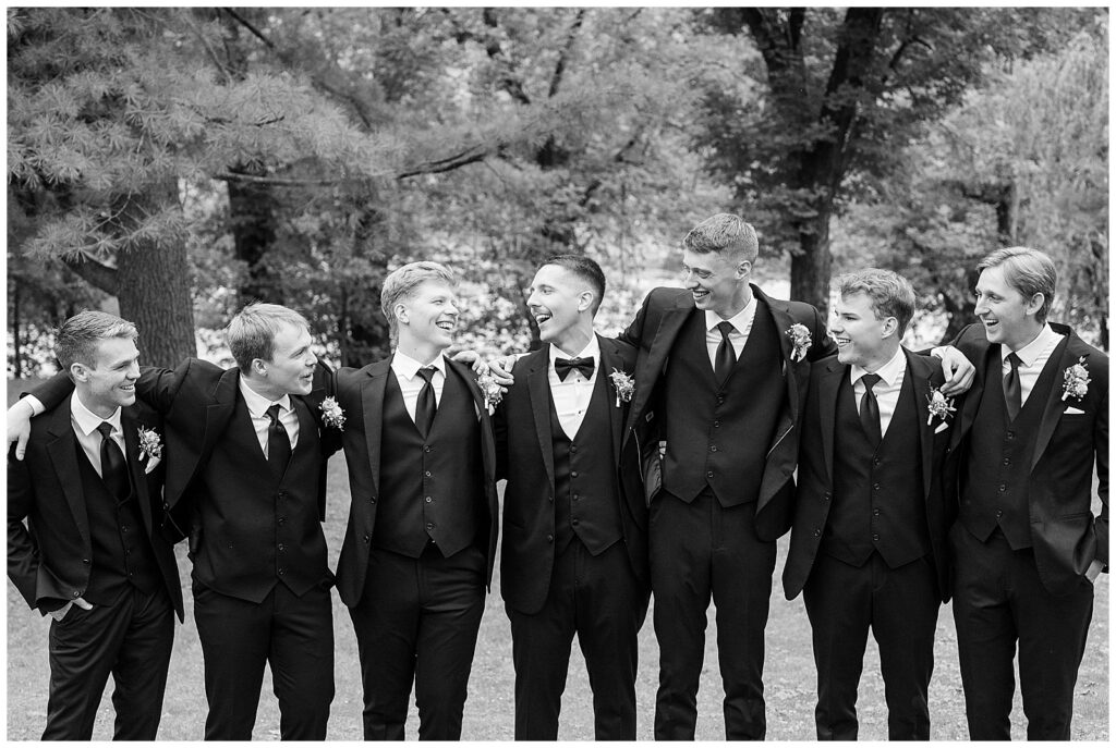 Black and white photo of groomsmen laughing with arms around each other at Riverdale Manor wedding