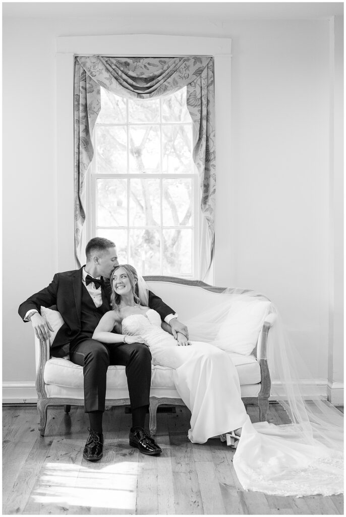 Black and white portrait of bride and groom on vintage settee by window at Riverdale Manor