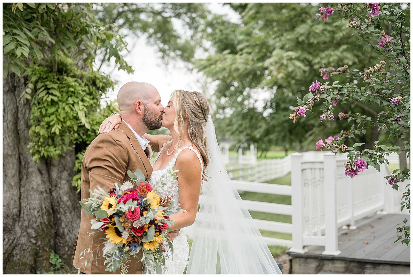 Bride and groom kissing in front of weeping willow and white fence at Barn at Silverstone Lancaster PA autumn wedding
