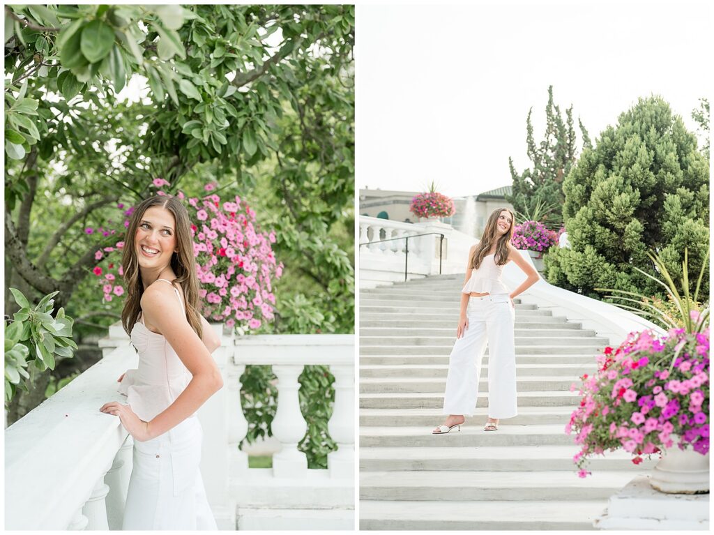 High school senior in a blush corset top and white wide-leg pants posing on the grand staircase at Hotel Hershey surrounded by pink hanging petunia baskets