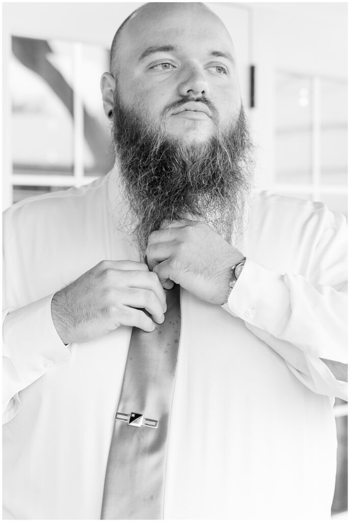 Black and white photo of Chris adjusting his silver tie and tie bar while getting ready