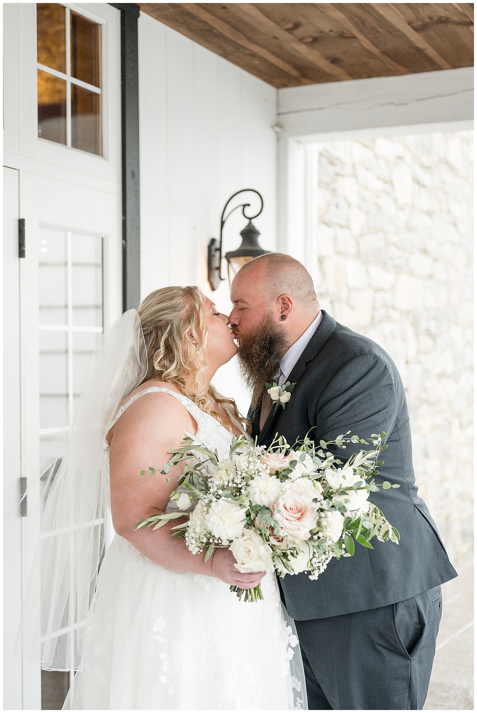 Rebecca and Chris kissing on the covered porch as she holds her blush and white bouquet